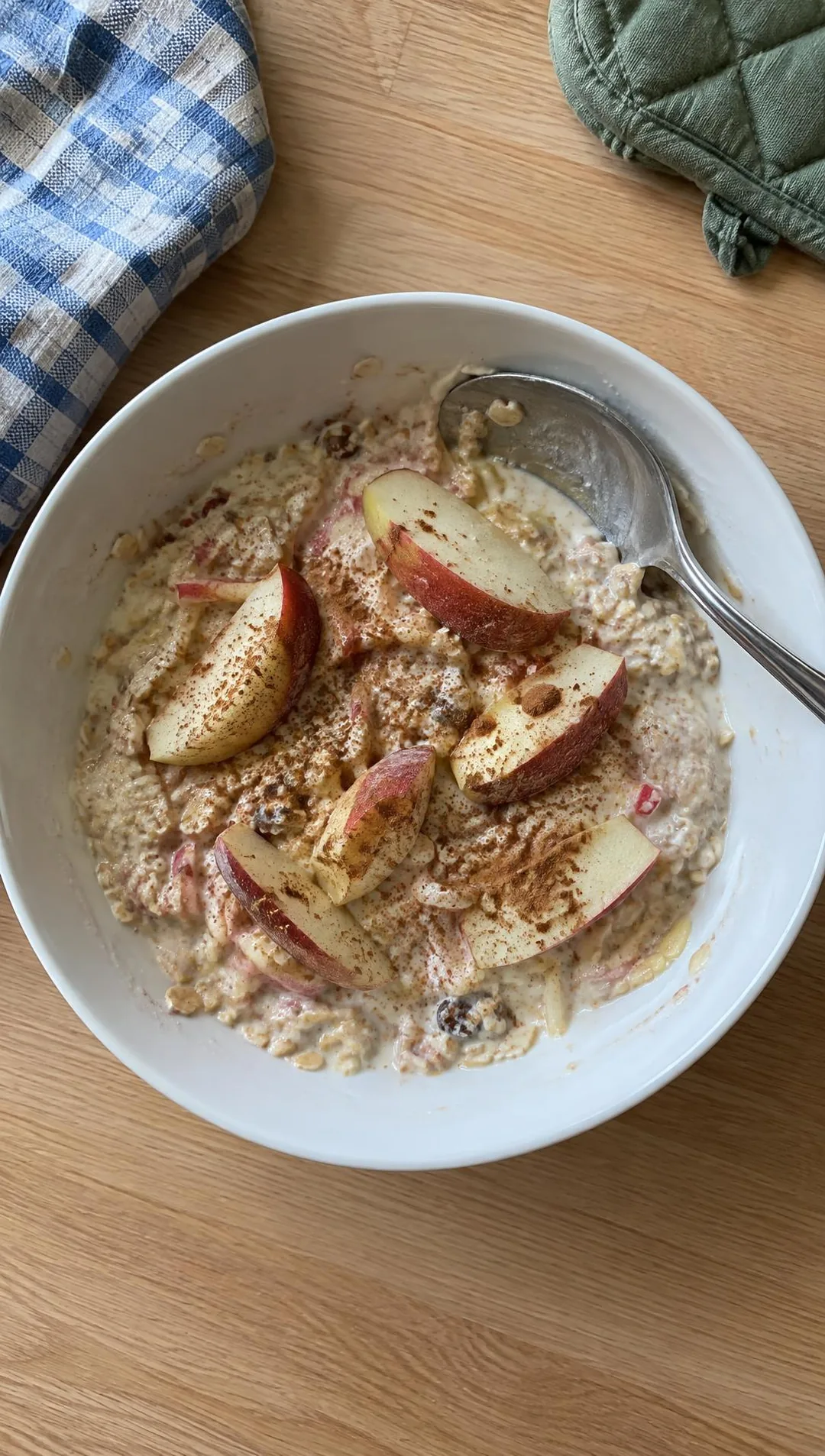 Schüssel mit cremigem Bircher-Müsli und Apfelspalten, eine Kinderhand taucht einen kleinen Löffel hinein