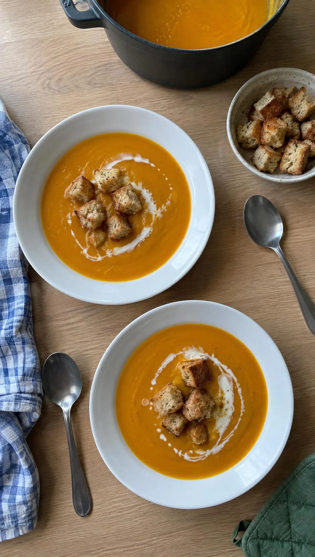 Kinderhand streut goldbraune Croûtons auf einen Teller mit orangefarbener Kürbissuppe