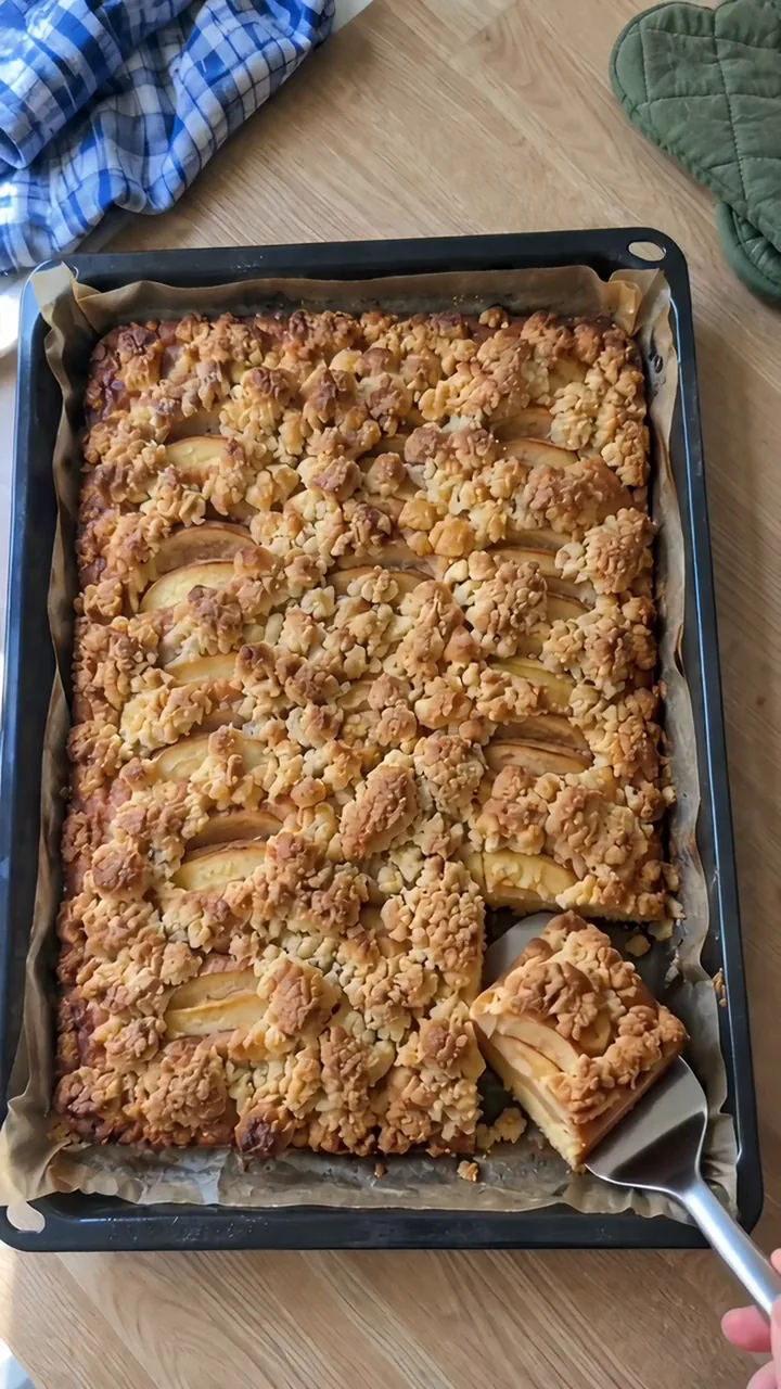 Ein Pfannenwender aus Metall hebt ein geschnittenes Stück Kuchen aus dem Blech, einige Krümel fallen herunter