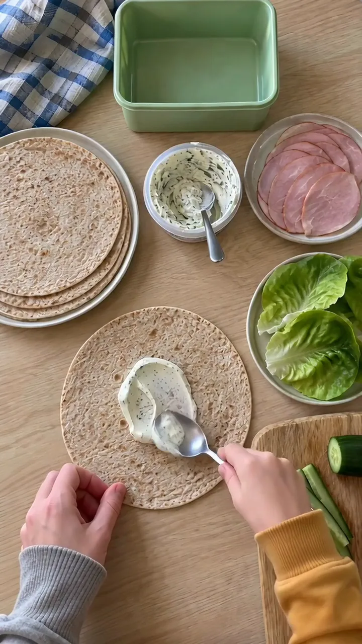 Kinderhand verstreicht Frischkäse mit dem Rücken eines Löffels auf einer Tortilla