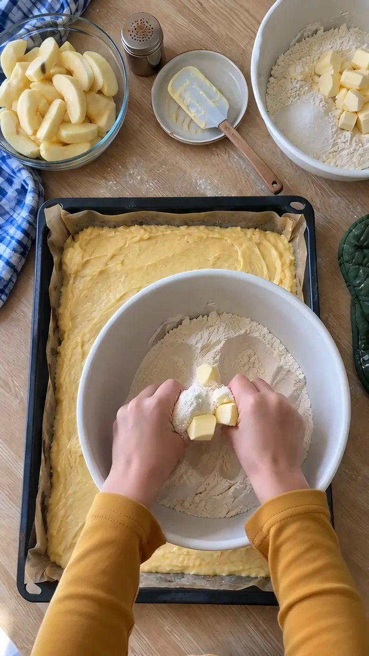 Zwei Kinderhände zerreiben Mehl, Zucker und Butterwürfel in einer weißen Schüssel zu groben Krümeln