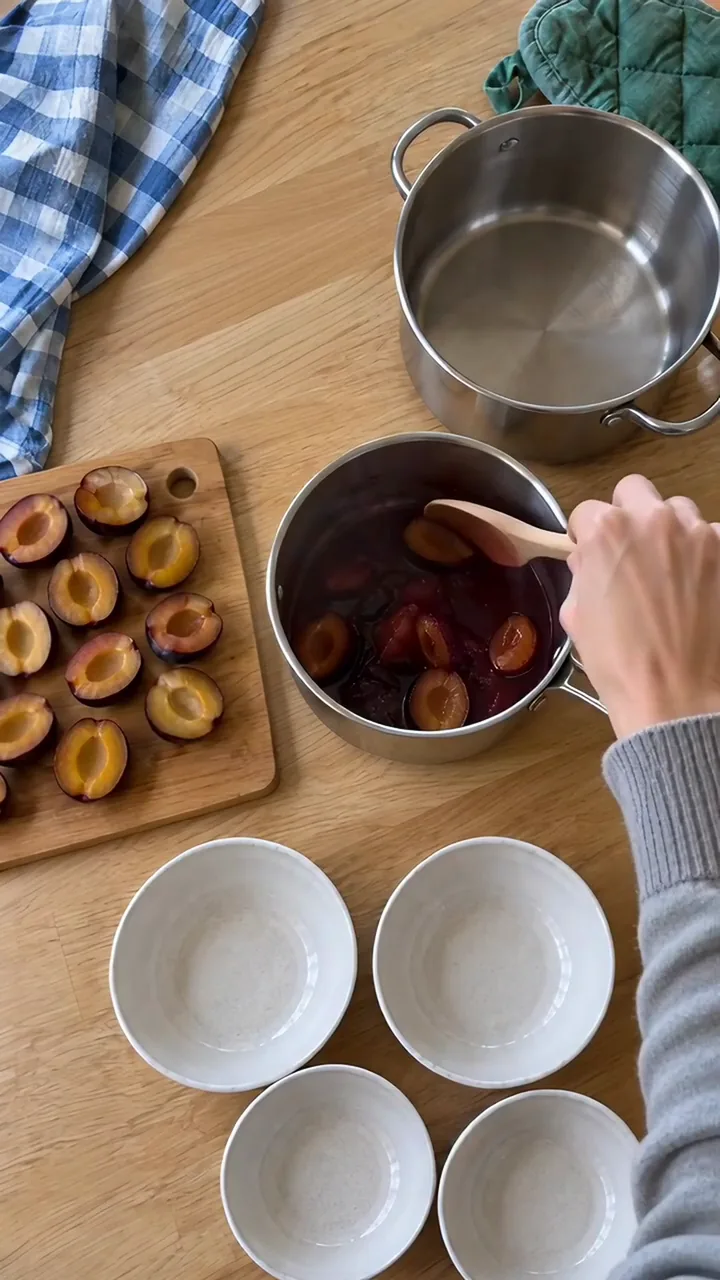 Erwachsene Hand rührt weiches, dunkles Zwetschgenkompott im Topf mit einem Holzlöffel um