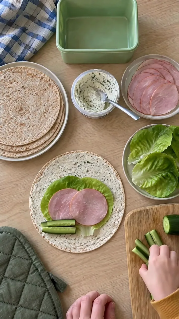 Kinderhand legt lange Gurkenstreifen entlang des unteren Randes der Tortilla