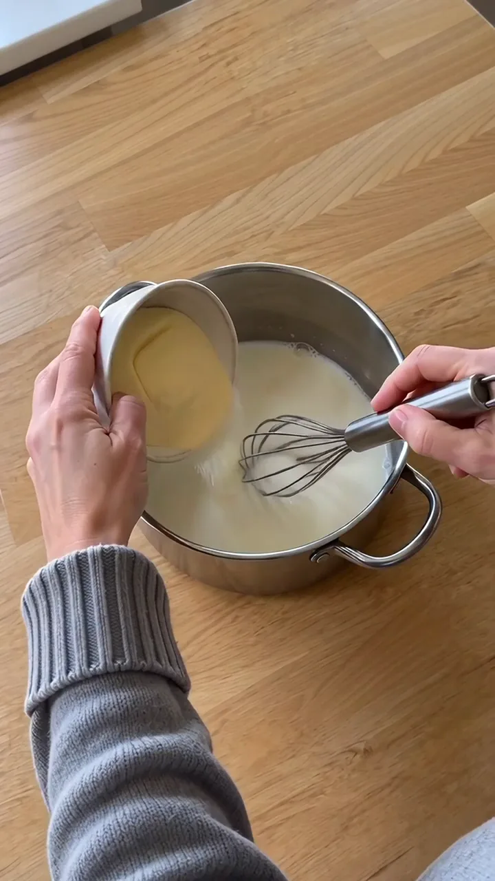 Erwachsene Person gießt Grieß aus einem kleinen Schälchen in heiße Milch und rührt dabei mit dem Schneebesen