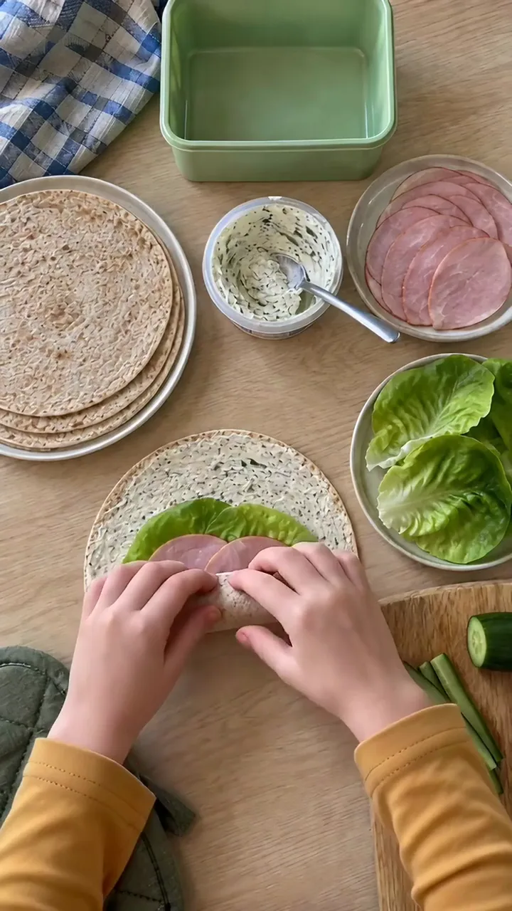 Zwei Kinderhände rollen den Wrap vom unteren Rand aus fest nach oben auf