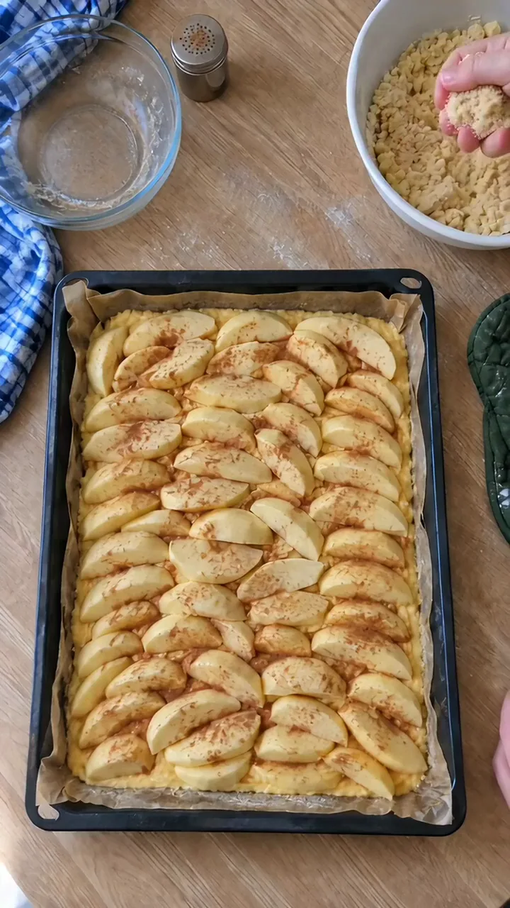 Eine Kinderhand lässt eine große Handvoll Streusel über die Äpfel auf dem Blech rieseln