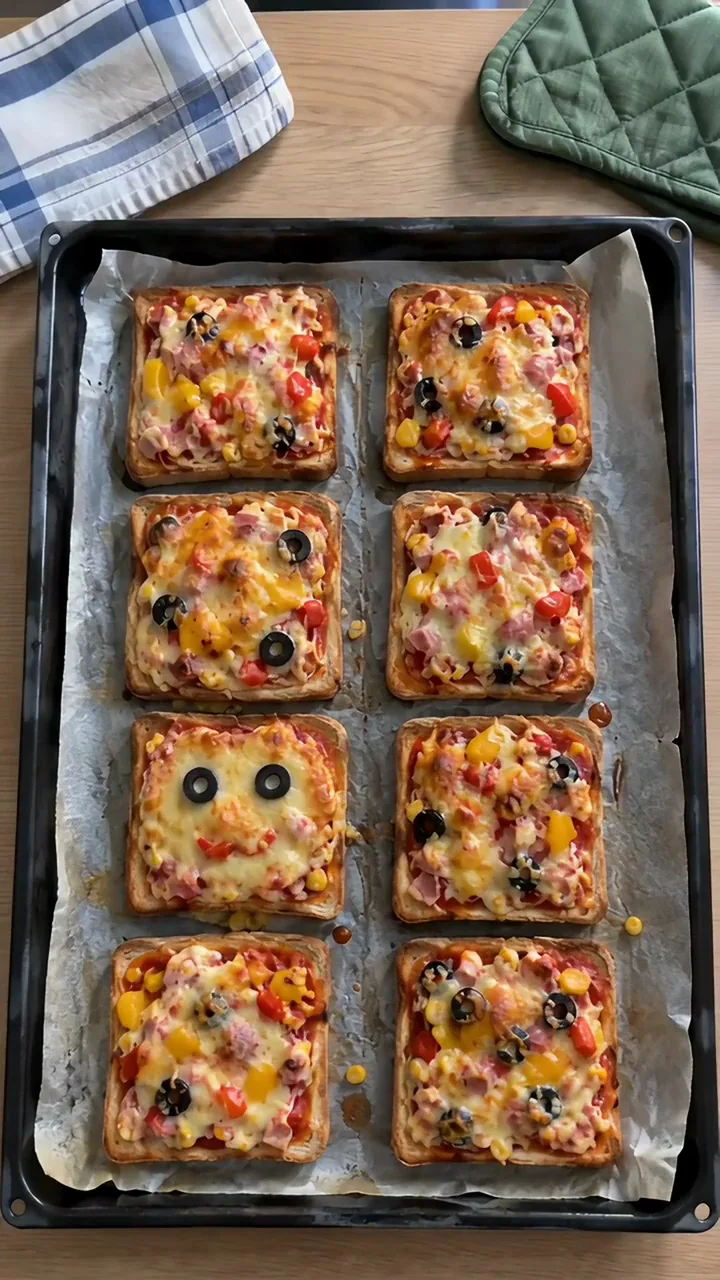 Backblech mit acht gebackenen Toast-Pizzen, der Käse goldbraun geschmolzen, eine Pizza hat zwei Olivenaugen