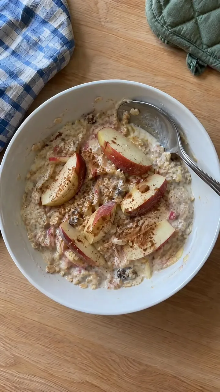 Kinderhand streut Zimt von einem Teelöffel über das eingeweichte Müsli mit Apfelspalten