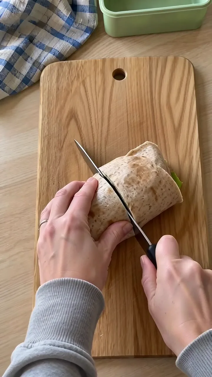 Erwachsenenhand schneidet die Wrap-Rolle auf dem Brett mit einem Messer schräg durch